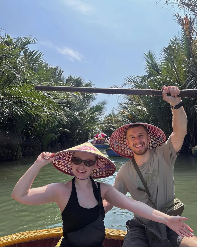 Couple in conical hats on a basket boat through Bay Mau Coconut Forest waterway Cam Thanh Hoi An — golden afternoon light