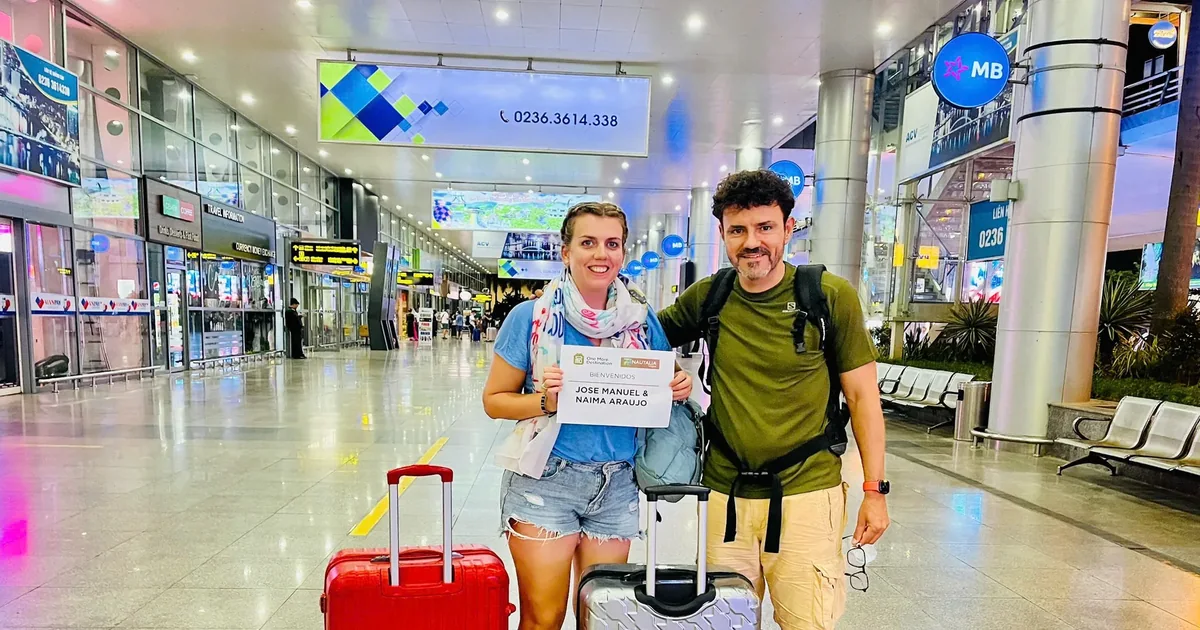Minh Vu Travel driver greeting guests at Da Nang Airport arrivals hall with welcome name board — private car transfer to Hoi An