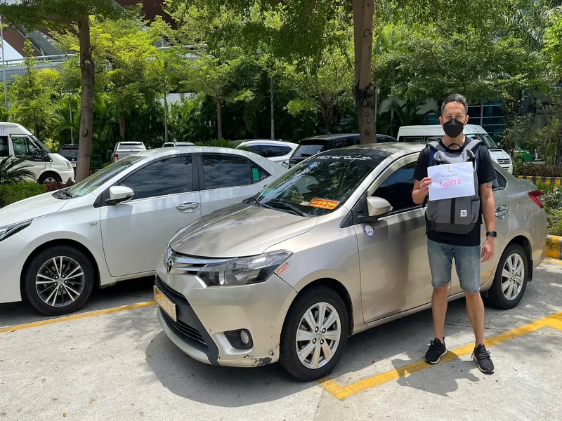 Private car driver holding welcome sign next to Toyota Vios sedan at Da Nang Airport — transfer to Hoi An