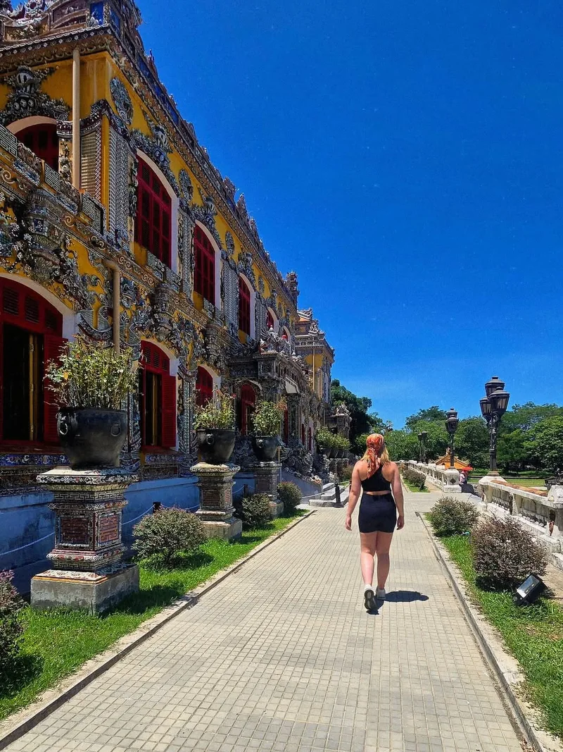 Walking past ornate imperial palace buildings inside Hue Citadel — yellow walls and elaborate decorations — day trip from Hoi An