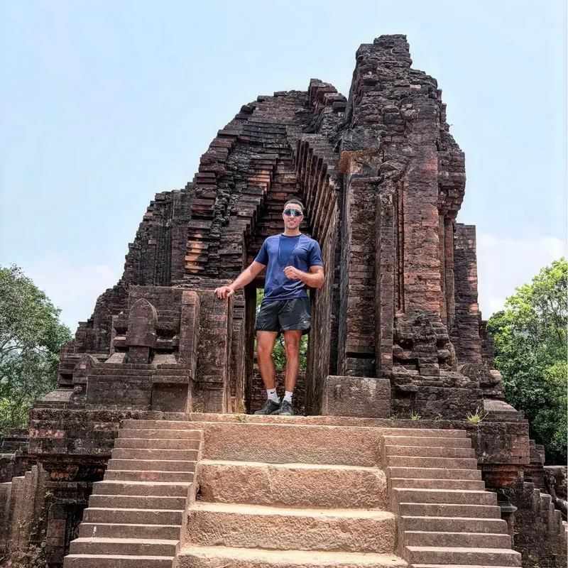 Visitor standing in the ruined archway of a Cham Hindu temple at My Son Sanctuary near Hoi An — best visited before 10 AM