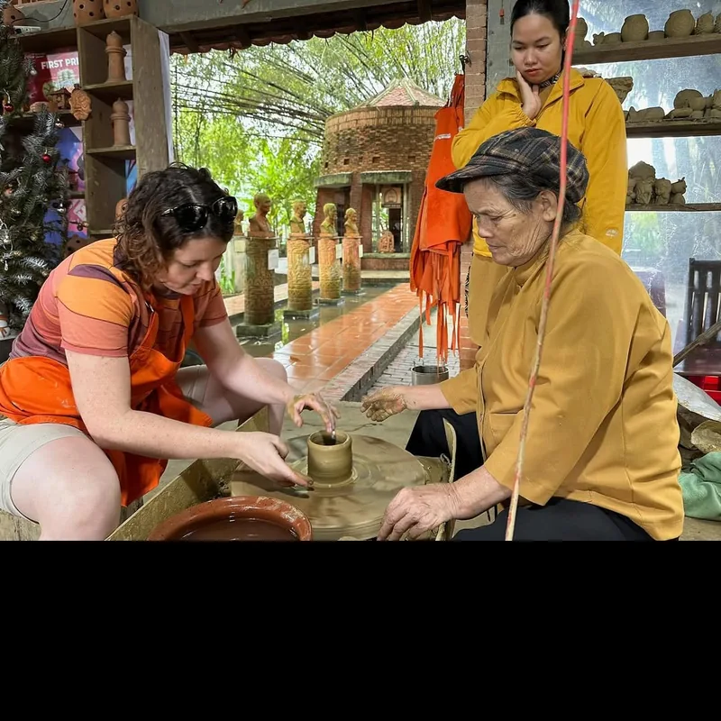 Elderly Thanh Ha pottery artisan teaching a foreign visitor to use the pottery wheel — hands-on workshop at the 15th-century village near Hoi An